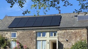 Una casa con techo solar, paredes de piedra y un porche delantero con sillas y plantas en macetas.