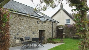 A stone house with a patio table and chairs, a small garden, and a wooden gate. - The Linhay (Okehampton)