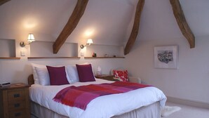 A bedroom with a large bed, wooden beams, two bedside lamps, a white rug, and a framed picture on the wall. - The Linhay (Okehampton)