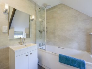 A modern bathroom with a glass-enclosed shower, a white vanity with a mirror, and a blue towel hanging on the bathtub.