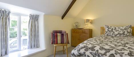 A bedroom with a bed, a wooden dresser, a window with curtains, and a fan on the dresser.