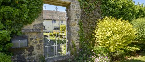 A stone building with a metal gate, surrounded by lush greenery and flowering plants.