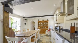 Uma cozinha com mesa e cadeiras de madeira, forno embutido e cafeteira.