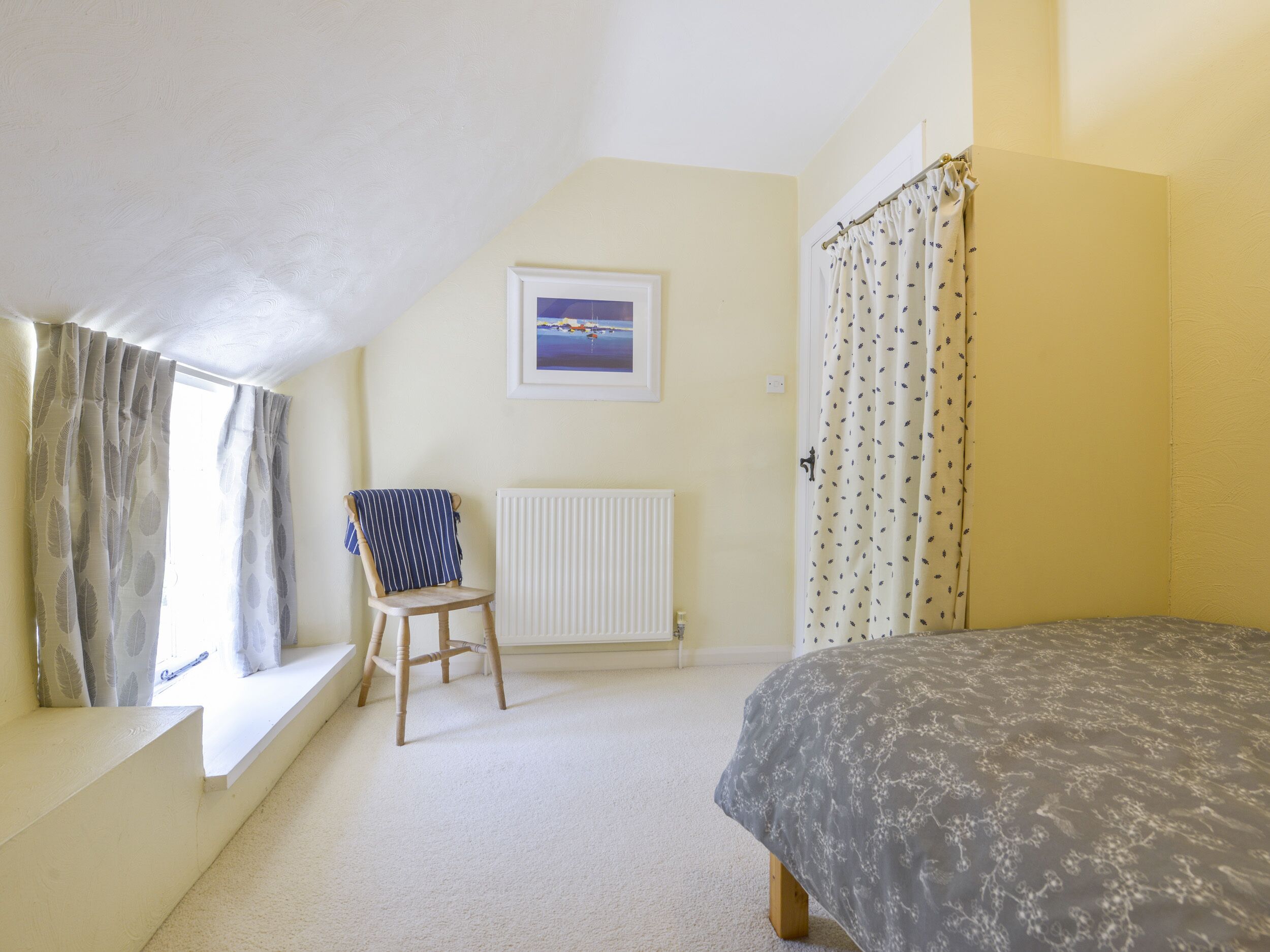 A bedroom with a bed, a chair, a radiator, and a window with curtains.