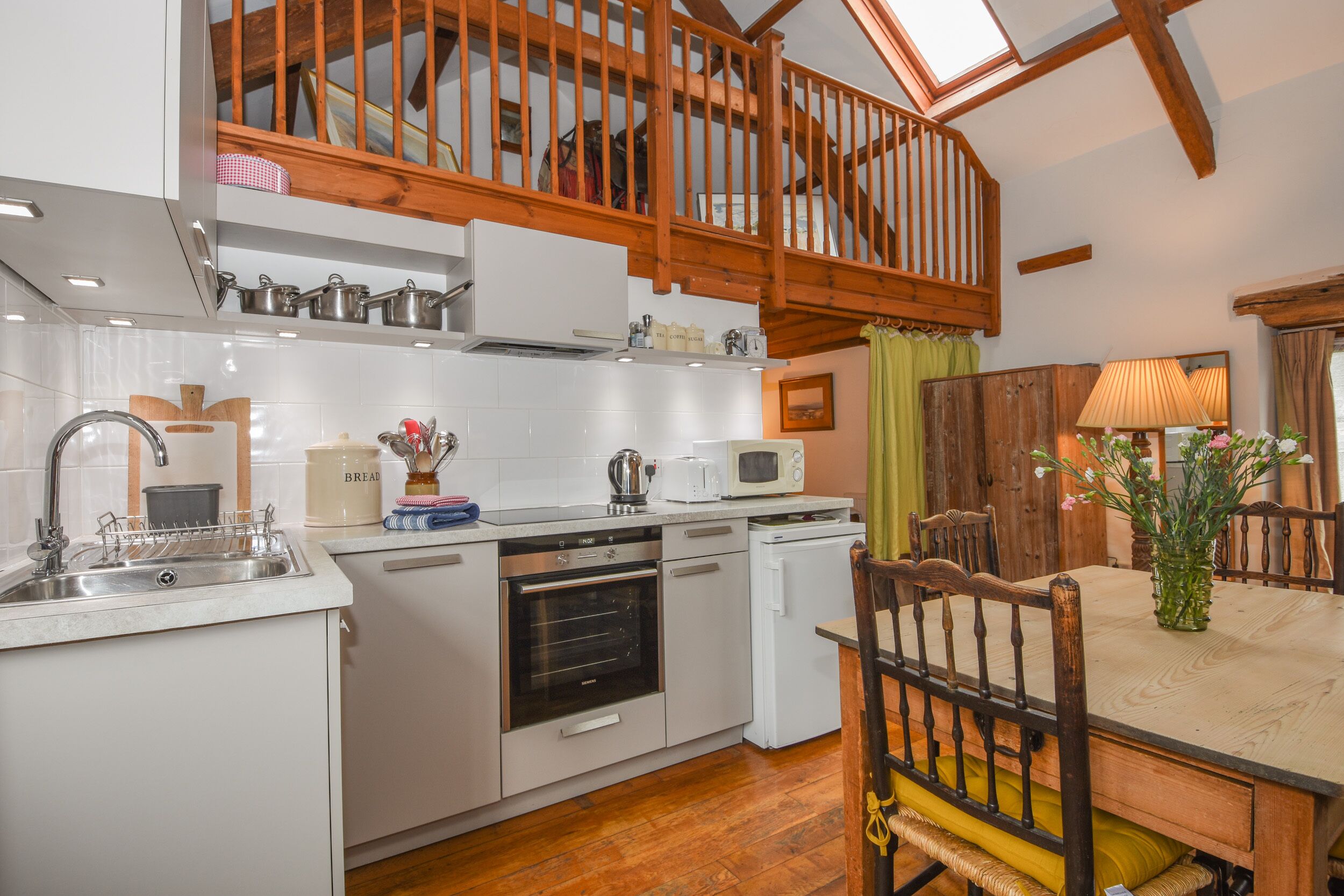 A modern kitchen with white cabinetry, a wooden staircase, and a dining area with a wooden table and chairs.