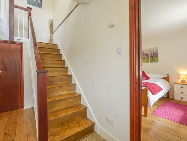 A staircase leading to a bedroom with a bed, bedside table, and a wall-mounted light. - Ludgate Cottage (Newton Abbot)
