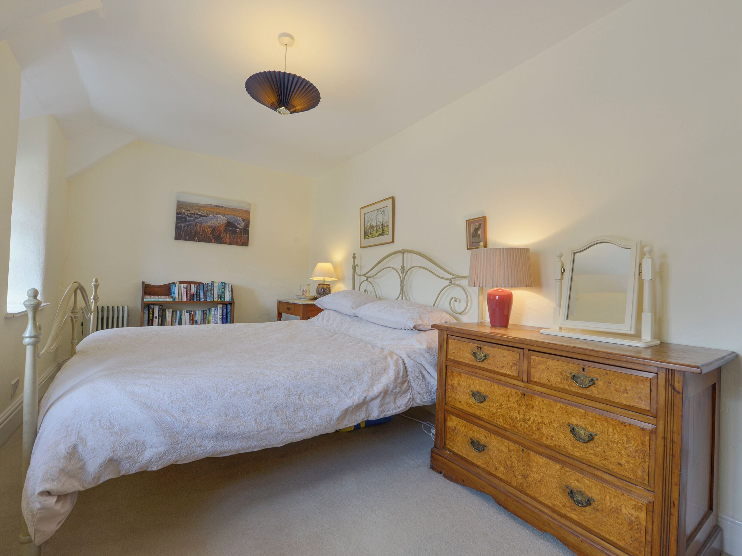 Une chambre à coucher comprenant un lit, une commode, une table de chevet, une lampe et un luminaire au plafond.