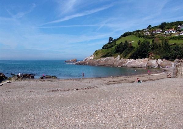 A pebble beach with houses on a hillside in the background.