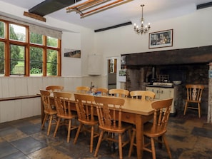 A dining area with a wooden table and chairs, a chandelier, a fireplace, and a window with a view of greenery.