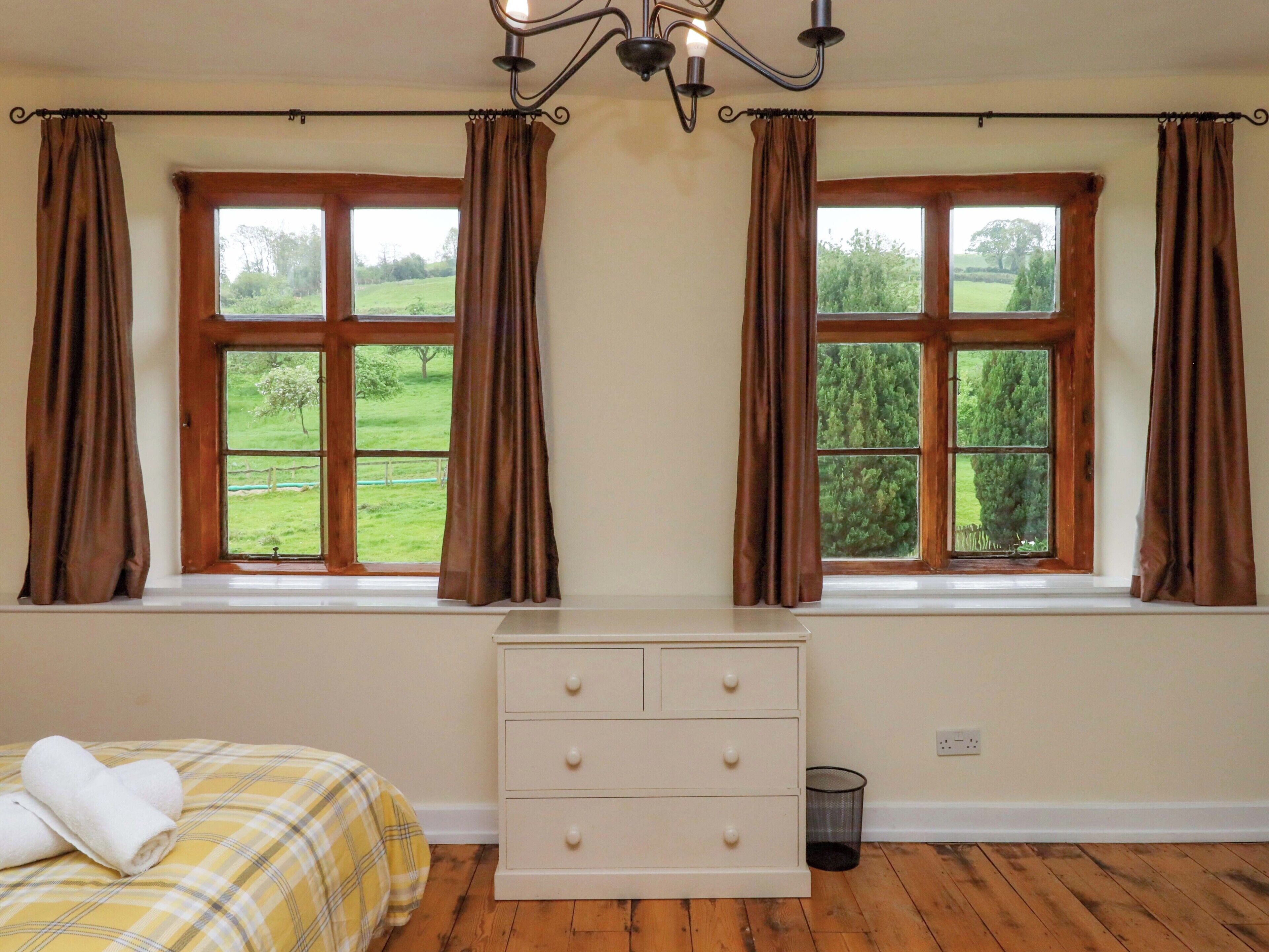 A bedroom with two windows, a bed, a dresser, and a chandelier.