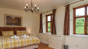 Un dormitorio con cama, candelabro, ventana con cortinas, un cuadro en la pared y suelo de madera.
