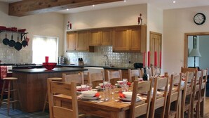 A modern kitchen with wooden cabinets, a central island, and a dining area set for six. - The Barn (Colyton)