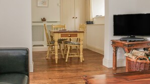 A dining area with a wooden table and chairs, a television on a wooden stand, and a wicker basket. - Alice Cottage (Minehead)
