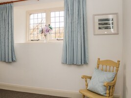 Una habitación con ventana, cortinas, una silla y un cuadro en la pared.