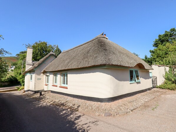 A traditional thatched-roof house with a white exterior, a chimney, and a small window with a green frame.