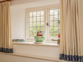 Ein Fenster mit Blick auf Grün, eine tassenförmige Tasse mit grünen Punkten auf einer Fensterbank und ein Bücherstapel.