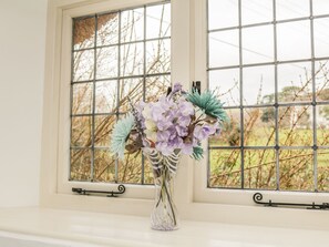 A window with a metal grid, a vase with flowers, and a view of trees outside.