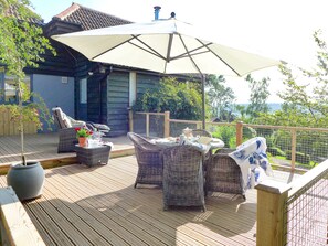 A wooden deck with wicker furniture and a large umbrella, overlooking a scenic landscape.