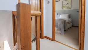 A wooden staircase leading to a bedroom with a bed, a nightstand, and a wall-mounted lamp.