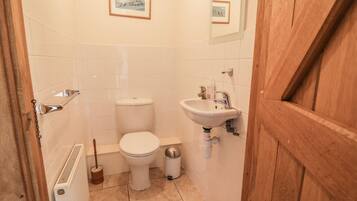 Une petite salle de bain propre, équipée de toilettes, d’un lavabo et d’un radiateur. Des tableaux encadrés ornent le mur, et la porte est en bois.