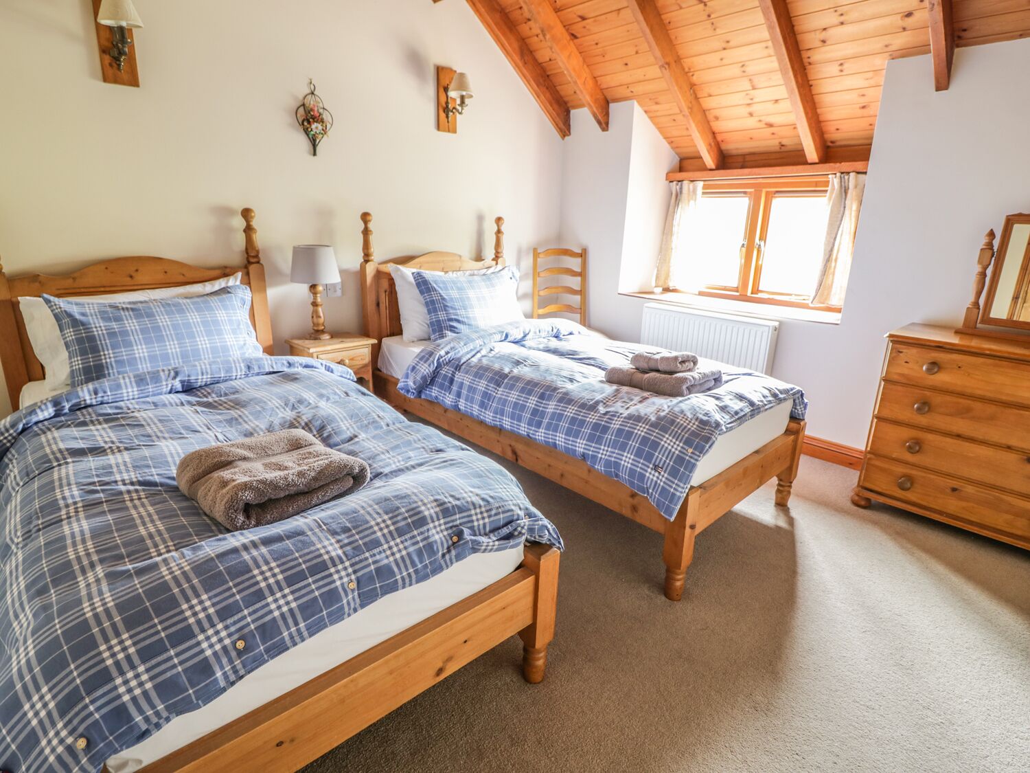 A bedroom with two wooden beds, a dresser, and a window with curtains.