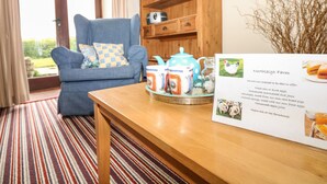 A cozy room with a blue armchair, a wooden cabinet, and a table with a teapot and cups. There's a sign about Northleigh Farm offering fresh eggs and homemade jams. - The Linney (Colyton)