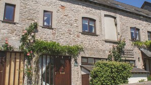 A stone building with multiple windows, a wooden door, and a small garden with pink flowers. - Linney Cottage (Dartmouth)