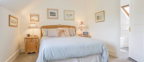 A bedroom with a bed, two bedside tables, a lamp, and framed pictures on the wall.