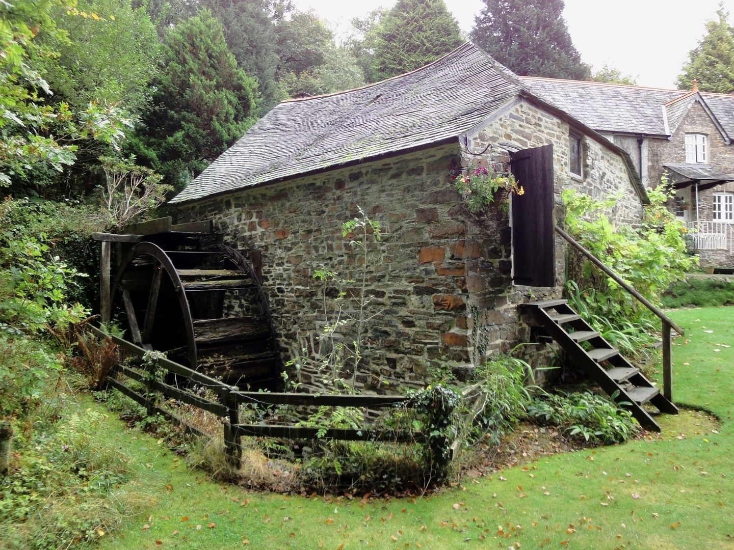 A stone building with a water wheel and a staircase leading to a door.