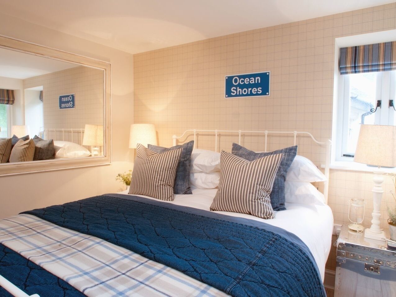 A hotel room with a bed, a nightstand, a mirror, and a sign that reads "Ocean Shores".