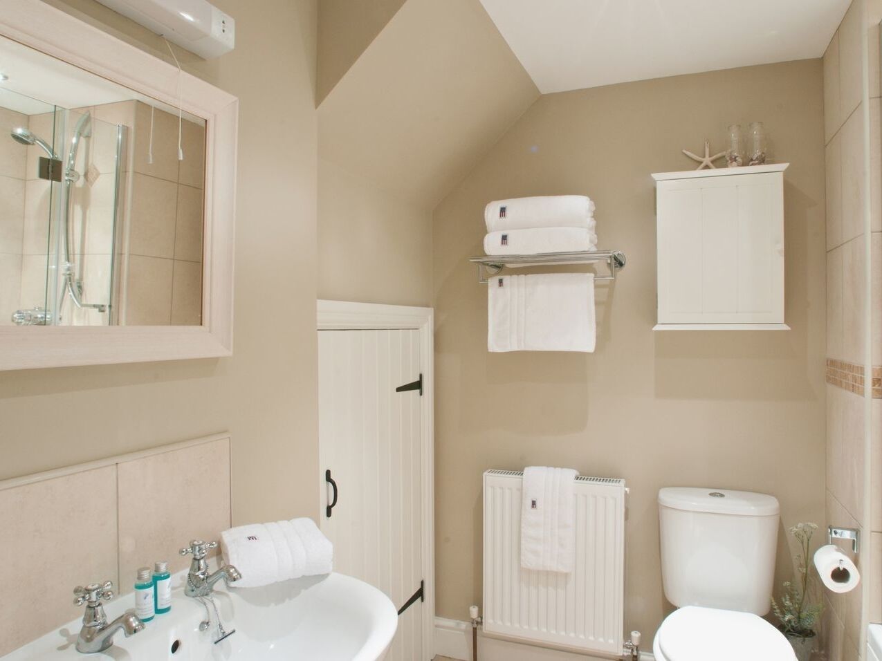 A bathroom with a sink, mirror, shower, toilet, and towel racks.