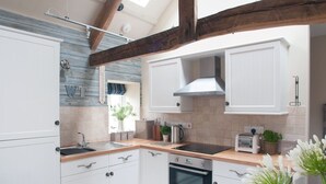 A modern kitchen with white cabinetry, a wooden countertop, a built-in oven, and a stainless steel range hood. - Saltwind Granary (Bideford)