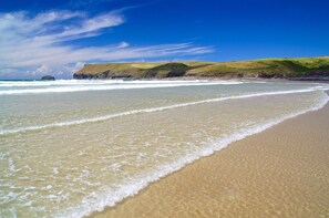 A beach with clear blue water, sandy shore, and grassy hills in the background. - Chapel Cottage (Bideford)