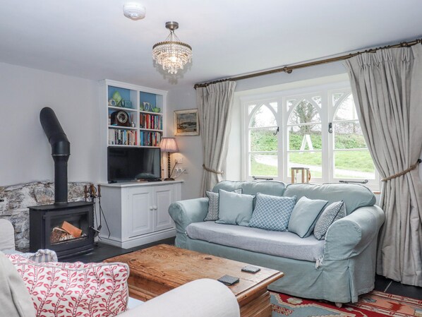 A cozy living room with a fireplace, a sofa, a wooden coffee table, and a bookshelf. - Chapel Cottage (Bideford)