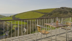 A terrace with a table and chairs overlooking a green landscape and the sea. - Ayrmer House (Kingsbridge)