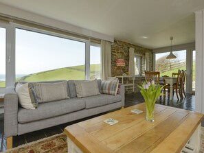 A modern living room with a grey sofa, a wooden coffee table, and a view of the countryside.