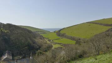 A rural landscape with rolling hills, a clear sky, and a distant view of the sea.
