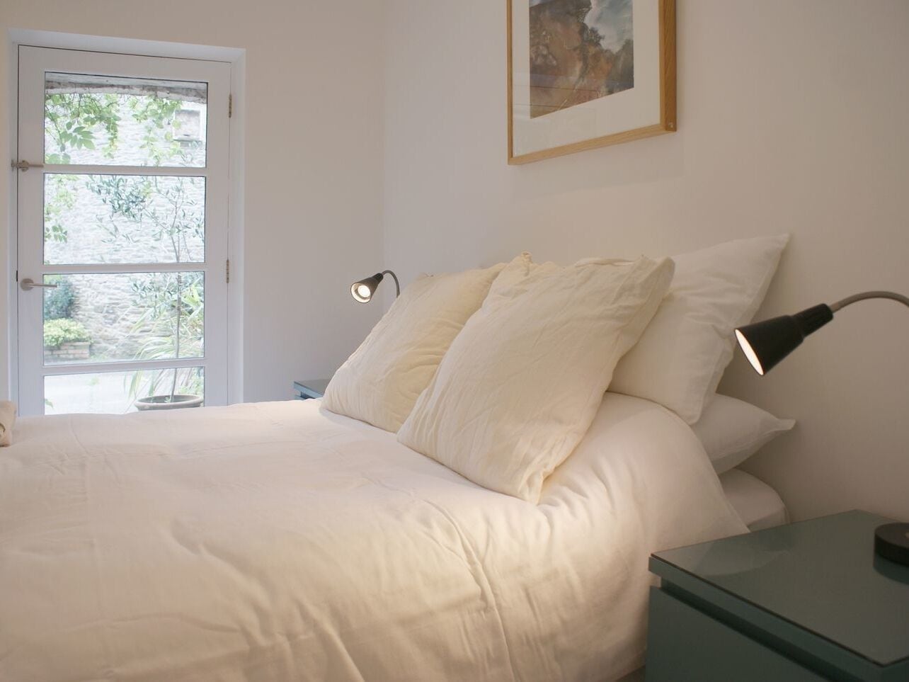 Een slaapkamer met een bed, nachtkastje, lamp en een deur naar buiten.