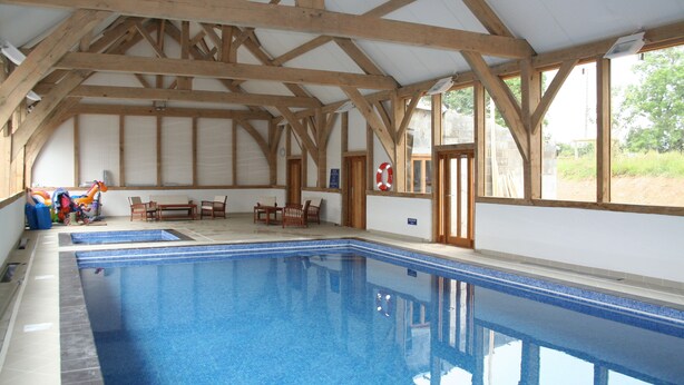 An indoor swimming pool with wooden beams, a lifebuoy, and a view of the outdoors.