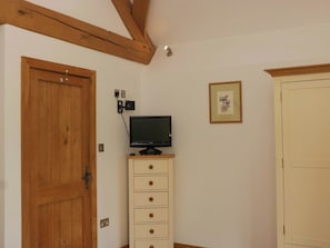 Une pièce avec une porte en bois, un téléviseur posé sur une commode, un tableau encadré au mur et une armoire blanche.