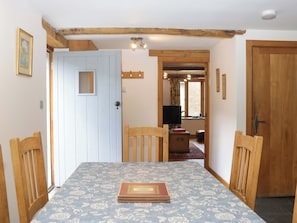 A dining area with a table, chairs, a door, and a television in the background. - The Hay Barn (Totnes)