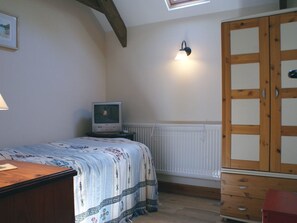 Cozy bedroom with a sloped ceiling and exposed beams, featuring a single bed, table, chair, TV, and wardrobe.