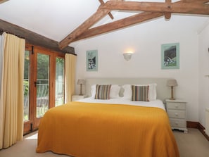 A bedroom with a bed, two bedside tables, a window with curtains, and a ceiling with exposed beams.