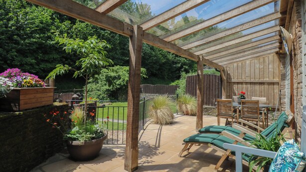 A covered patio with wooden furniture, a wooden fence, and potted plants.