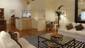 Un amplio salón con techo de madera, un sofá blanco, una mesa de centro y una cocina al fondo.