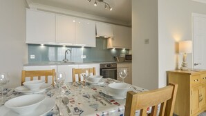 A modern kitchen with white cabinets, a built-in oven, and a dining area with a table set for four. - 3 Tarifa (Kingsbridge)