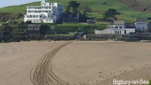 A coastal building with multiple floors, situated on a sandy beach with a hill in the background. - 3 Tarifa (Kingsbridge)