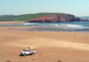 A lifeguard vehicle on a sandy beach with a rocky cliff and ocean in the background.