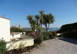 A gravel path leading to a garden with palm trees and a view of the sea.