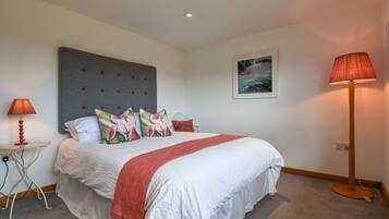 A neatly arranged bedroom with a large bed, a grey headboard, a red lamp, and a framed picture on the wall.